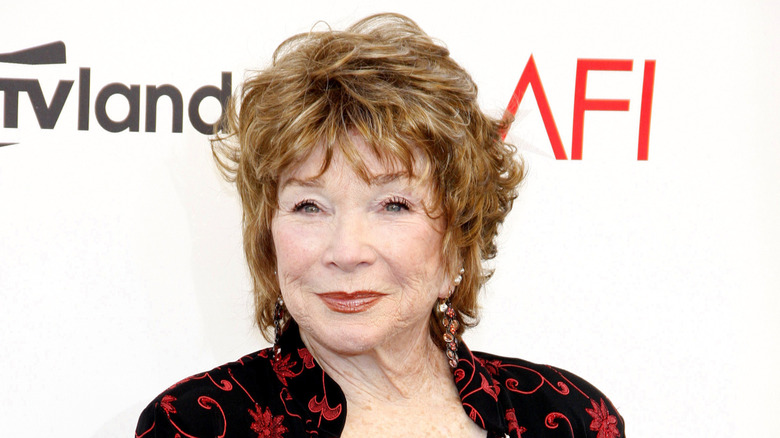 Shirley MacLaine posing in a black dress with red designs at the 40th AFI ceremony.