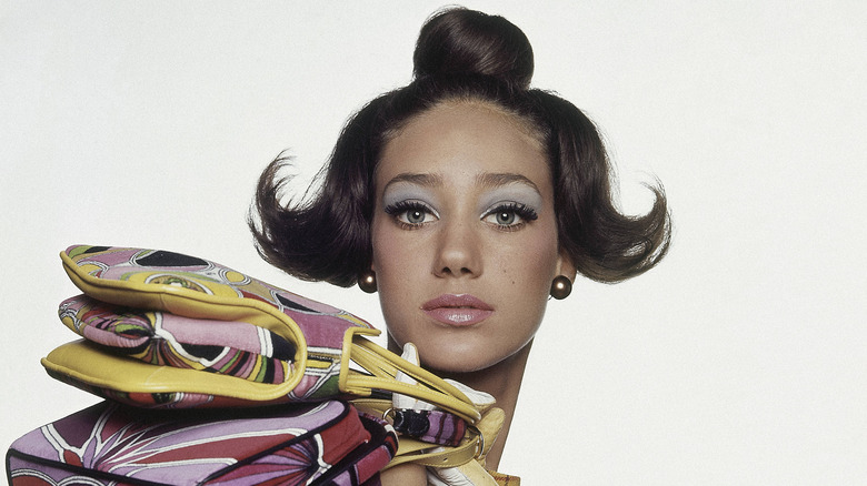 Model, Marisa Berenson, with three Pucci velveteen handbags over her shoulder, in a sleeveless yellow dress by Samuel Robert with yellow and white gloves by Fuchs, iridescent earrings by Laguna and chignon hairdo by Sebou for Revlon