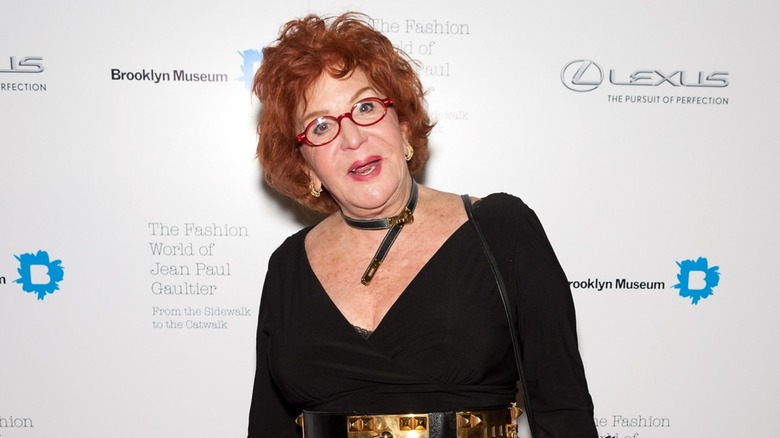 Sally Jessy Raphael wore a low-cut black top with a shiny gold belt and a matching belt necklace along with her short red hair and signature red glasses while attending The Fashion World of Jean Paul Gaultier in New York City in 2013.