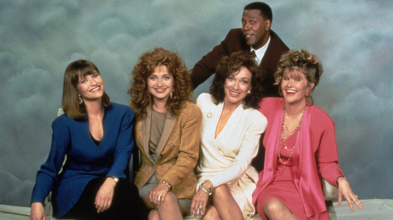 Jan Hooks, Annie Potts, Dixie Carter, and Judith Ivey sit on a bench smiling in front of Meshach Taylor