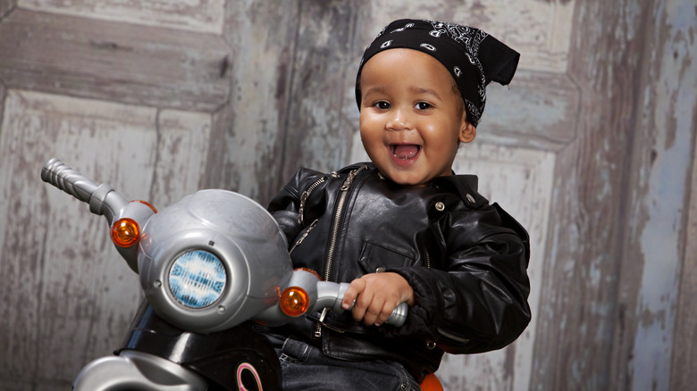 Baby in a leather jacket on a toy motorcycle