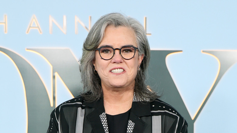 Rosie O'Donnell smiling and wearing a black jacket and glasses