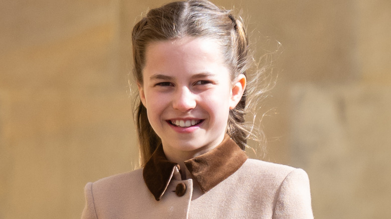 Princess Charlotte smiling, wearing beige and brown trench coat.