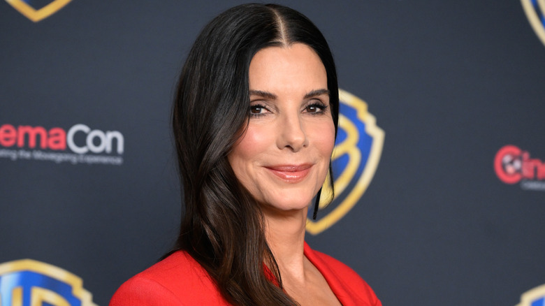 Sandra Bullock smiling at CinemaCon in a red suit with her hair down.