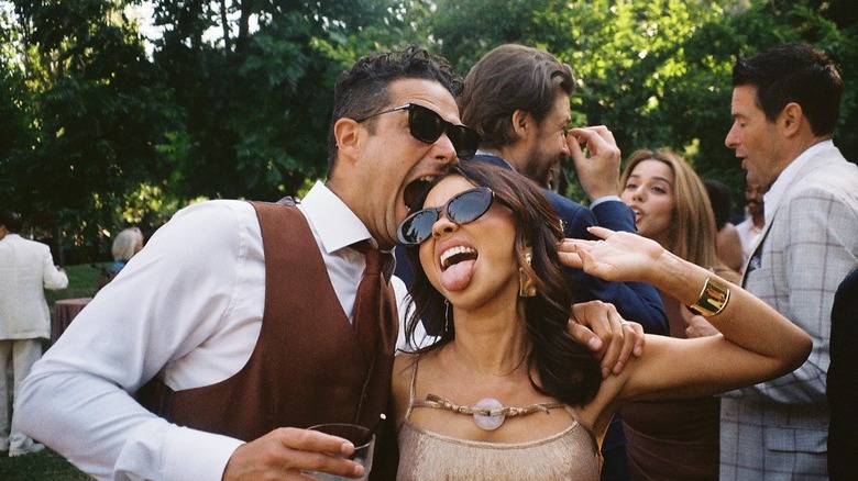 Wells Adams in a brown vest and tie with a white button down biting Sarah Hyland's head