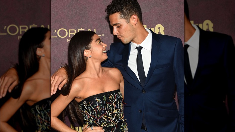 Sarah Hyland in a black dress with colorful details, hugging Wells Adams in a navy blue suit.