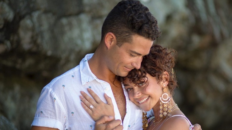 Wells Adams in a white button down shirt looking down at Sarah Hyland as they hug