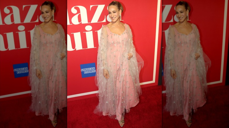 Sarah Jessica Parker smiling at a red carpet event wearing a flowing pink dress in 2022.