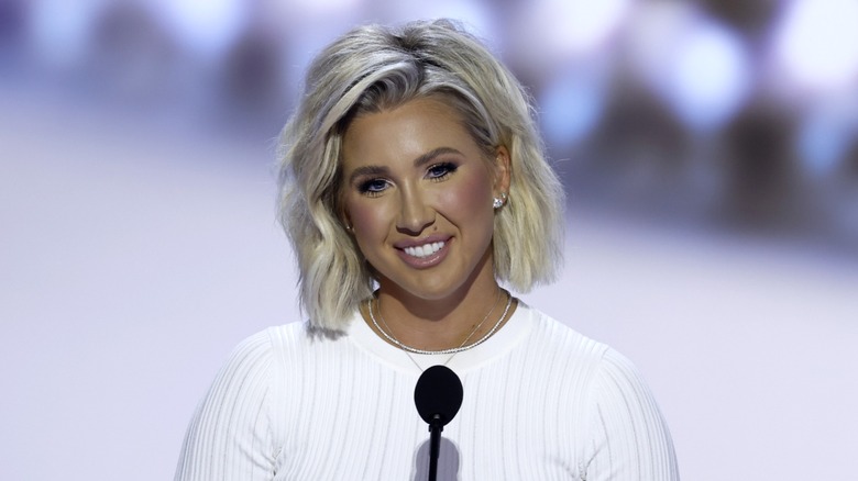 Close-up of Savannah Chrisley. She is wearing a face of makeup, overly done, and a white t-shirt.