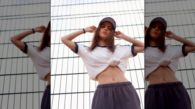 A woman posing in a white and navy blue knotted crop top and sweat pants.
