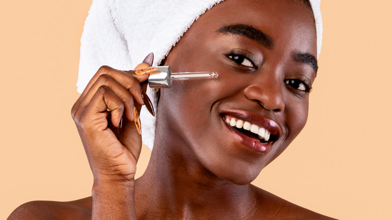 dark skin female applying skincare product to her face