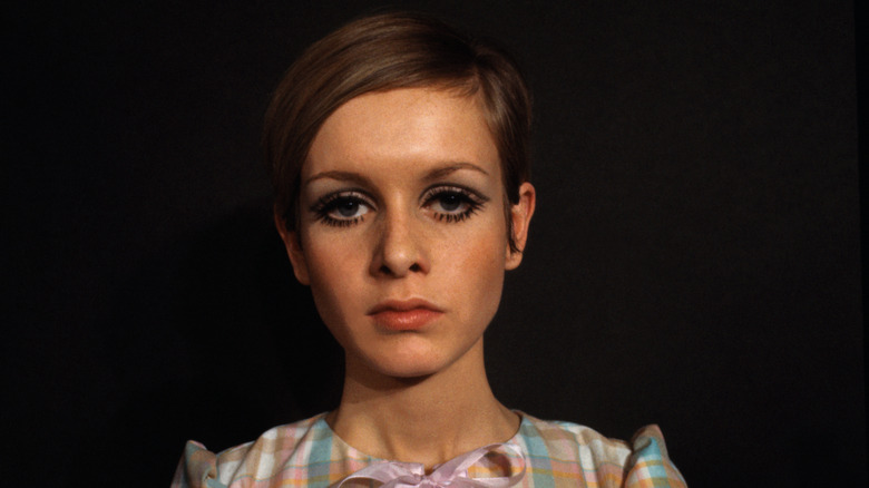 Twiggy poses wearing bold eyeliner and a pastel shirt.