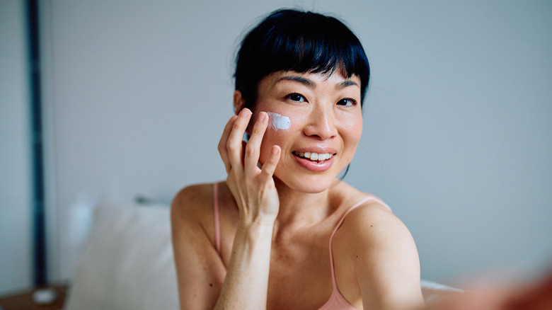 A woman applying a moisturizer while looking in the mirror to address skin complexion issues