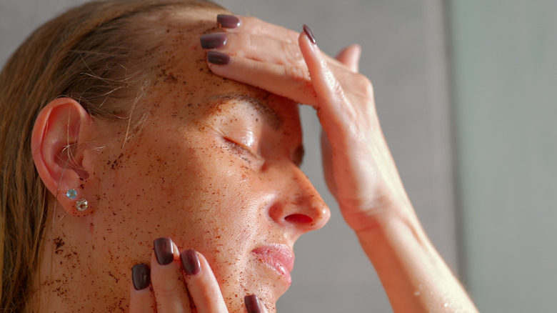 A woman using a physical scrub exfoliant on her face which might be too harsh for women in their 40s
