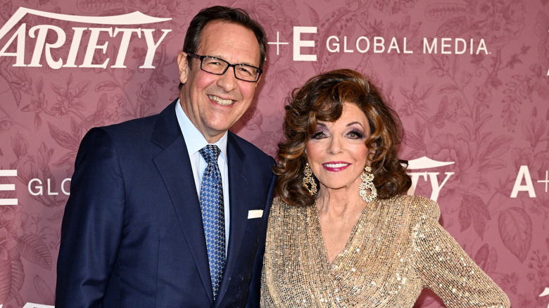 Percy Gibson(L) poses next to Joan Collins (R) who wears a gold sequin blouse
