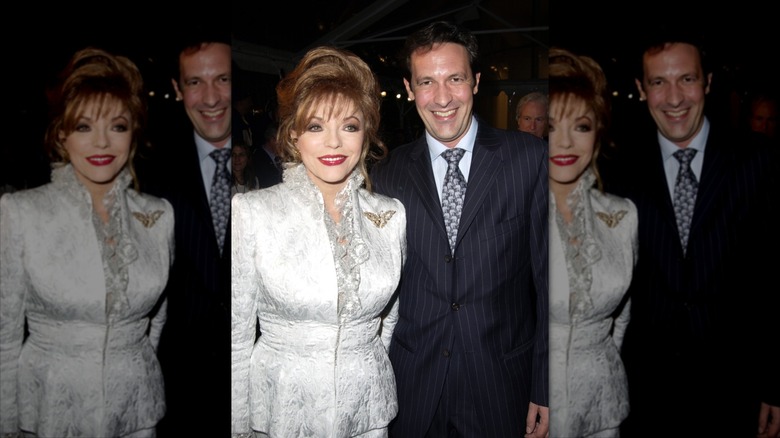 Joan Collins wearing a white skirt suit next to Percy Gibson in a suit