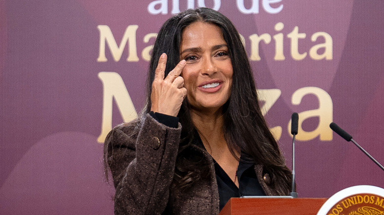 Salma Hayek speaking at a podium with her grays showing