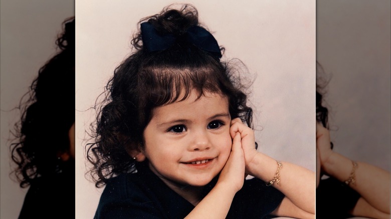 A baby-aged Selena Gomez poses with her hands on her cheek