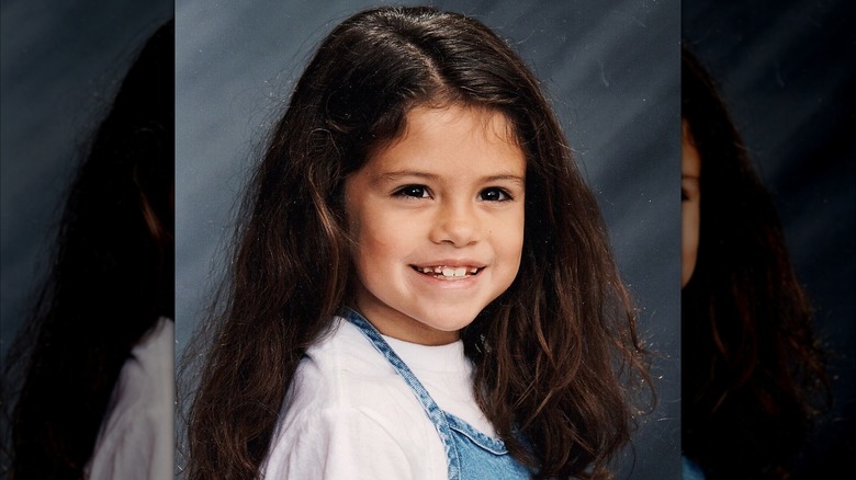 A young Selena Gomez in a white shirt and overall denim dress