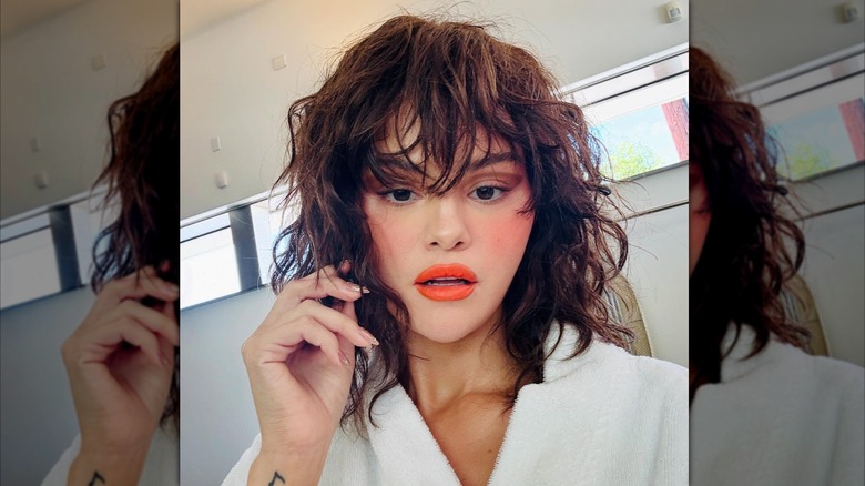 Selena Gomez poses in a robe with curly hair and orange lips