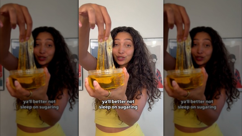 Instagram video still of Aliyah Marandiz wearing a yellow outfit and holding up a jar of Sugardoh hair removal product.