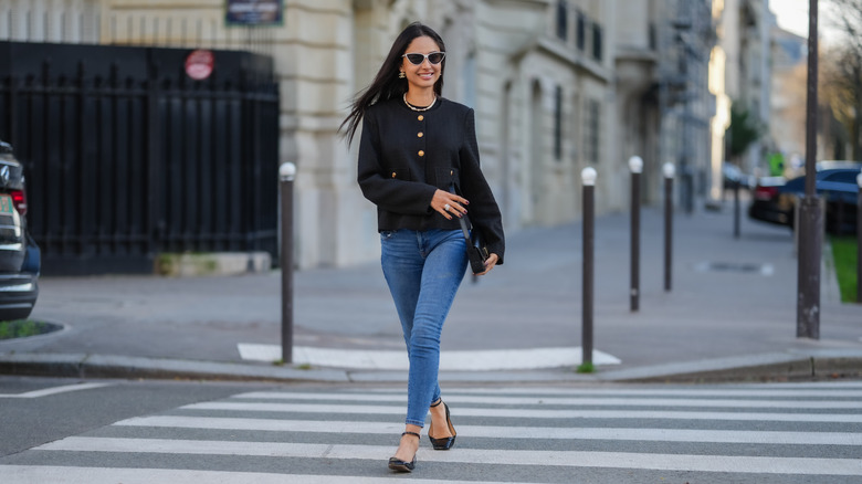 A woman walking across the road in skinny jeans which are outdated for summer 2026