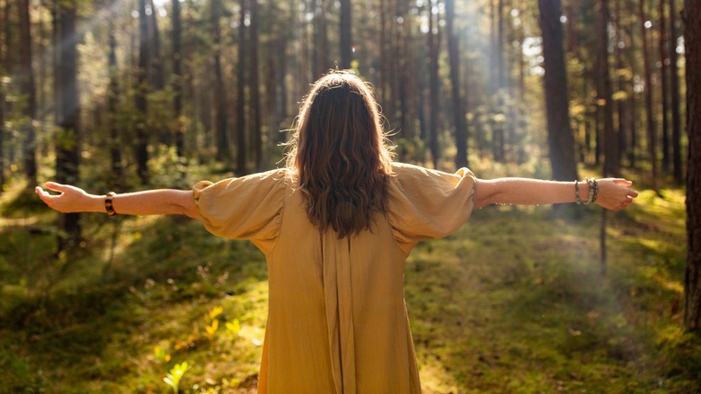Woman stands with arms out in forest sunbeam 
