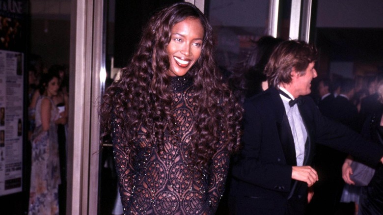 Naomi Campbell posing in an ornate black-lace dress with curly hair.