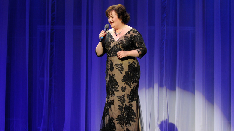 Susan Boyle holds a microphone wearing a black lace gown