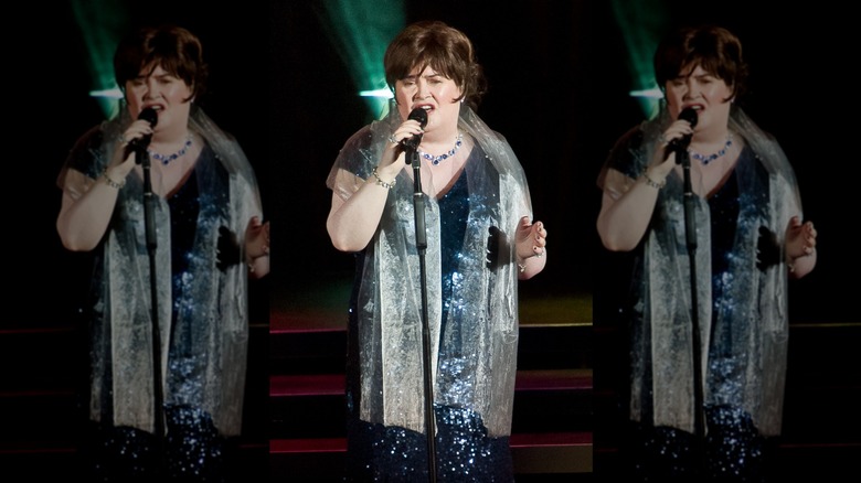 Susan Boyle sings into a microphone wearing a blue sequin dress