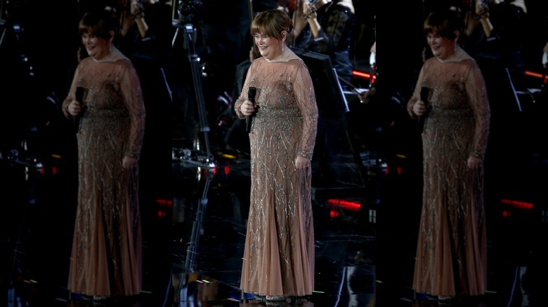 Susan Boyle holds a microphone wearing a sheer embellished gown