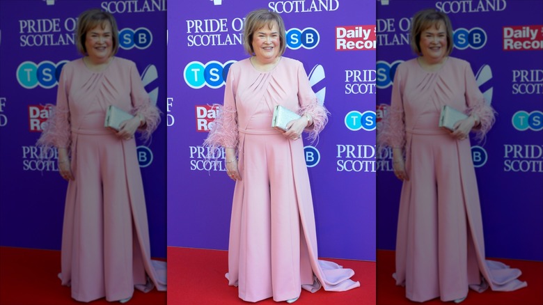 Susan Boyle smiles wearing a pink dress with feather cuffs