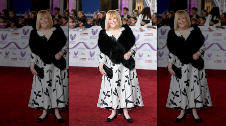 Susan Boyle smiles wearing a black fur shrug and a black-and-white dress