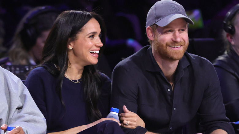Meghan Markle smiling siting next to Prince William with her arm in his.