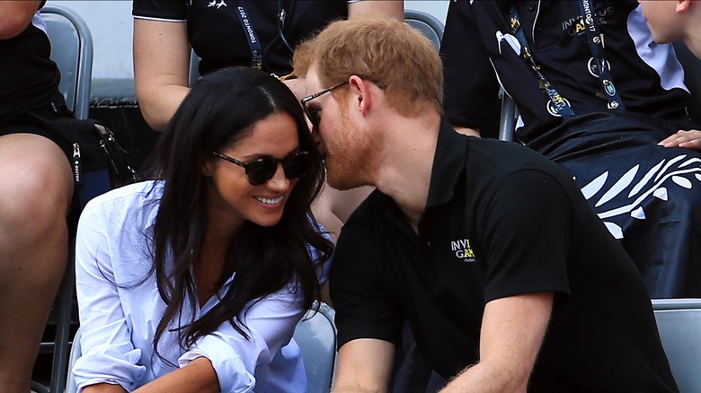 Prince Harry whispering in Meghan Markle's ear as she smiles at the 2017 Invictus Games.