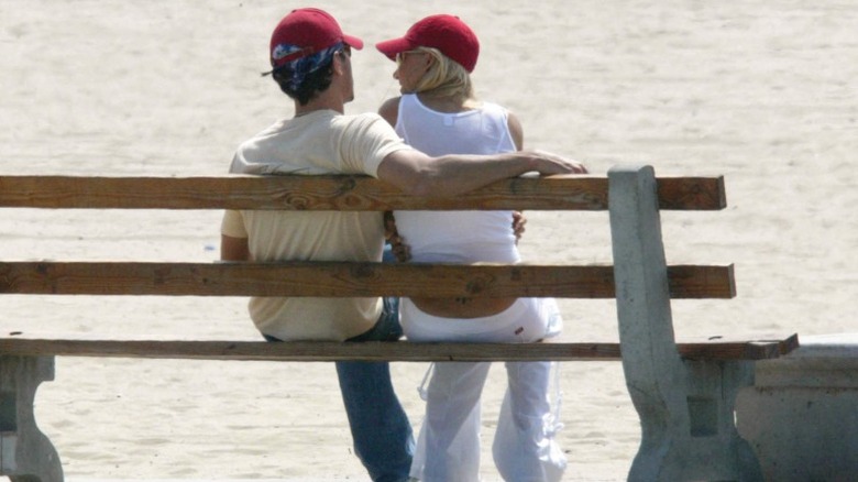 Anna Kournikova and Enrique Iglesias sit on a bench at the beach wearing red baseball caps