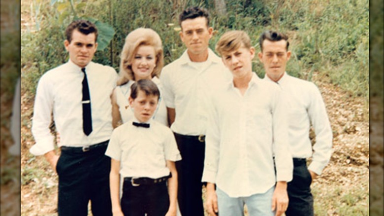 A young Dolly Parton is photographed with five of her six brothers wearing matching white outfits.