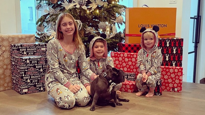 Siblings Taylor, Brayden and Hudson posing with their dog in front of a Christmas tree and presents wearing holiday pajamas.