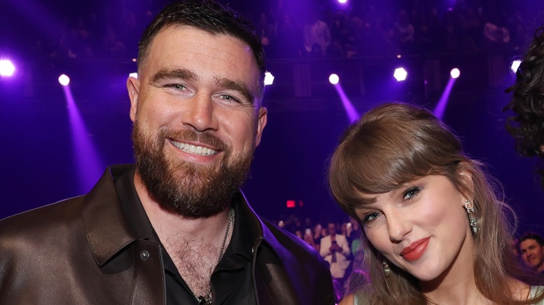 Taylor Swift and Travis Kelce smile and pose together while attending an award show ceremony