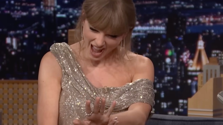 Taylor Swift beams while looking down at her engagement ring during a late-night TV appearance.