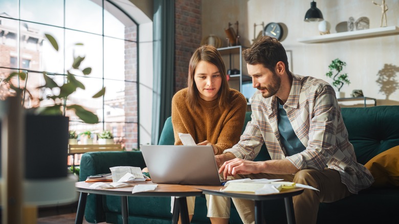 Couple surrounded in paperwork work together on laptop