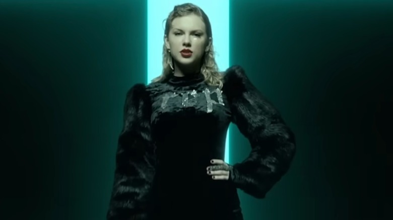 Taylor Swift wears a black fur bodysuit with long sleeves and the word 