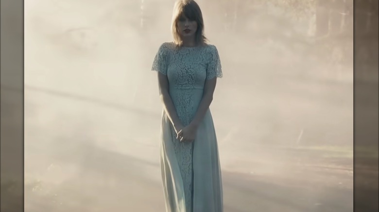 Taylor Swift stands alone in a long, pale blue dress with short lace sleeves.