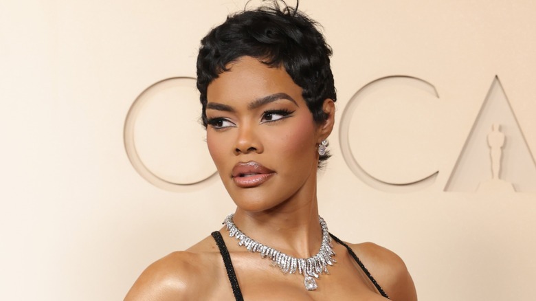 Close-up of Teyana Taylor on the 2026 Oscars red carpet. She is a woman with brown skin and a dark brown pixie cute. She is wearing a full glam makeup look and diamond earrings.