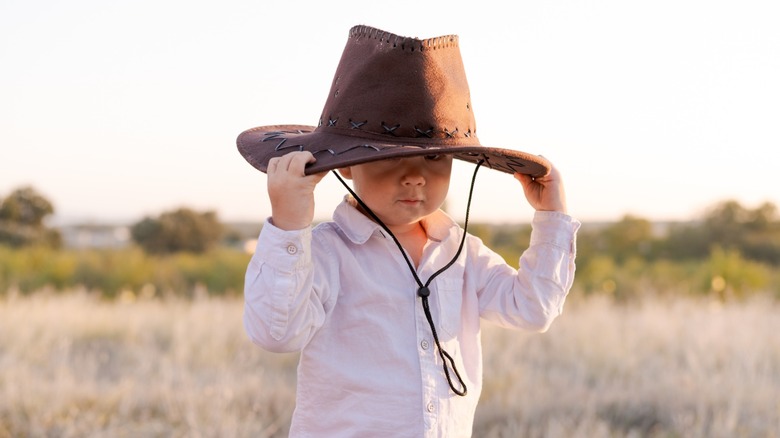 A baby holds a cowboy hat on his head.