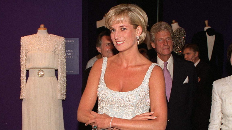 Princess Diana in a champagne-colored Catherine Walker dress standing with her arms crossed.