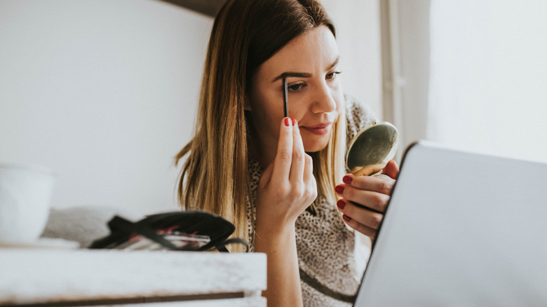 Woman doing eyebrows in handheld mirror