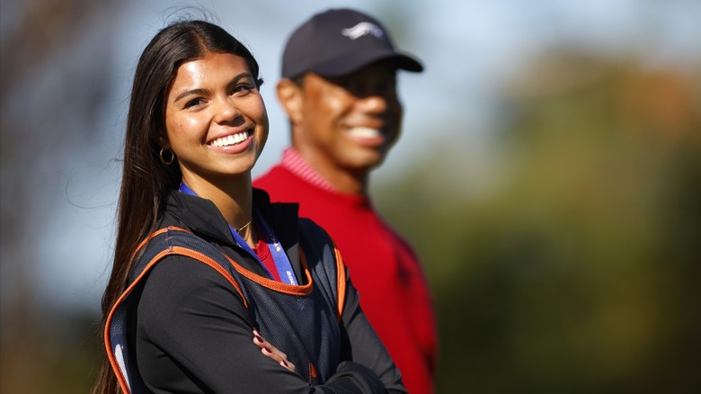 Sam Woods wears her long black hair down with small hoop earrings and a black jacket while standing at the first tee with father Tiger Woods during the PNC Championship in Orlando, Florida in December 2024.