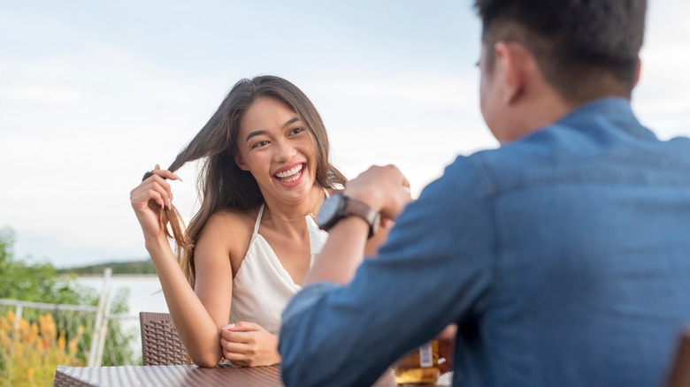 Woman twirling hair at table with man