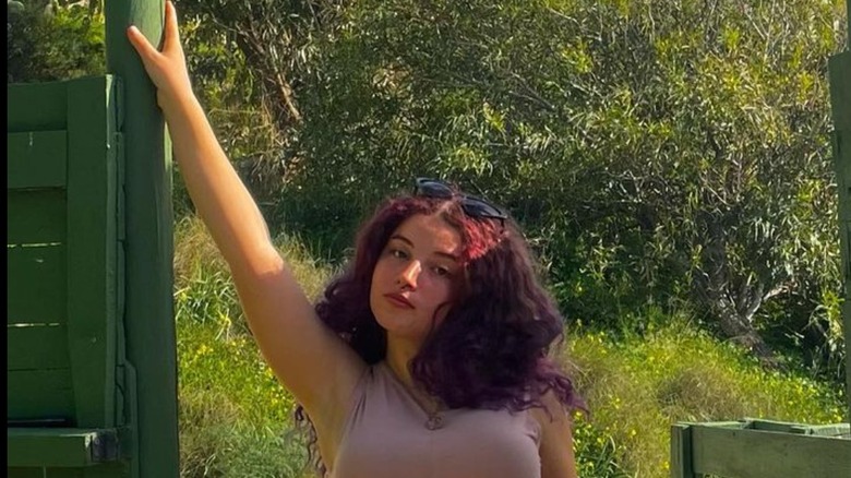 Woman poses against fence with curly blackberry hair 
